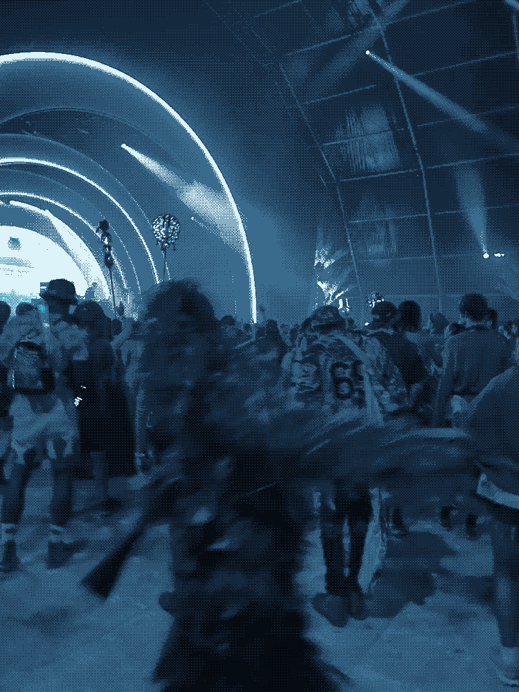 a blurred figure in a ghillie suit moving through a crowd under purple stage lighting